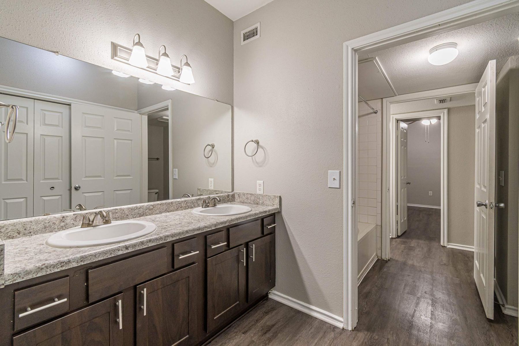 Empty room with wood floors, ceiling fan, and sliding glass door leading to a patio with vertical blinds at Apex West Midown.